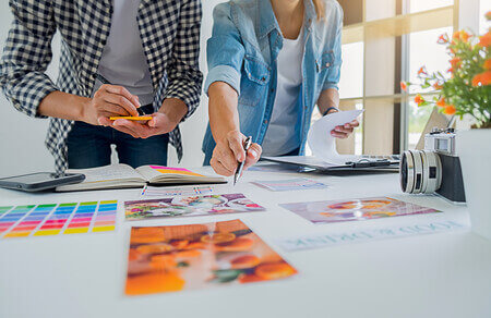 Two people brainstorming with woman pointing to printed materials on table